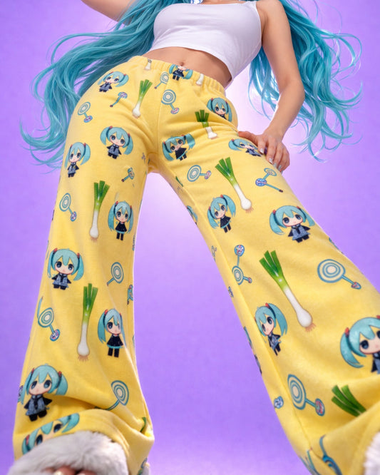 Low angle front view of yellow Hatsune Miku chibi pyjama bottoms with all over character and leek print, women’s anime fleece lounge trousers studio image