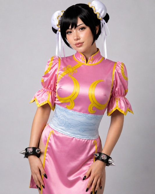 A woman modeling a pink and light blue Chinese-style costume dress with gold trim, white hair accessories, and spiked wrist cuffs against a plain gray studio background.
