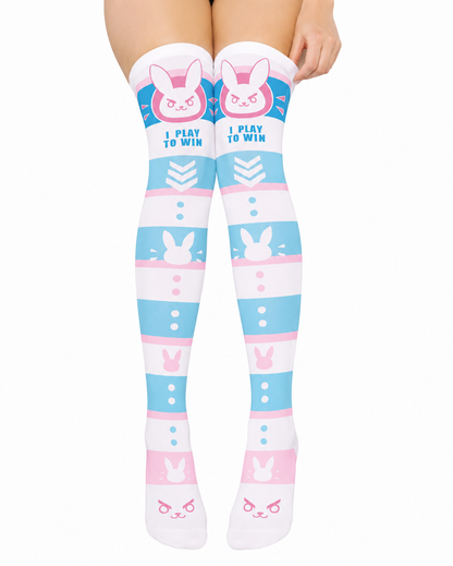 Over-the-knee socks with a pastel blue, pink, and white bunny-themed pattern and the text 'I PLAY TO WIN' on the upper leg, shown on a model's legs against a white background.