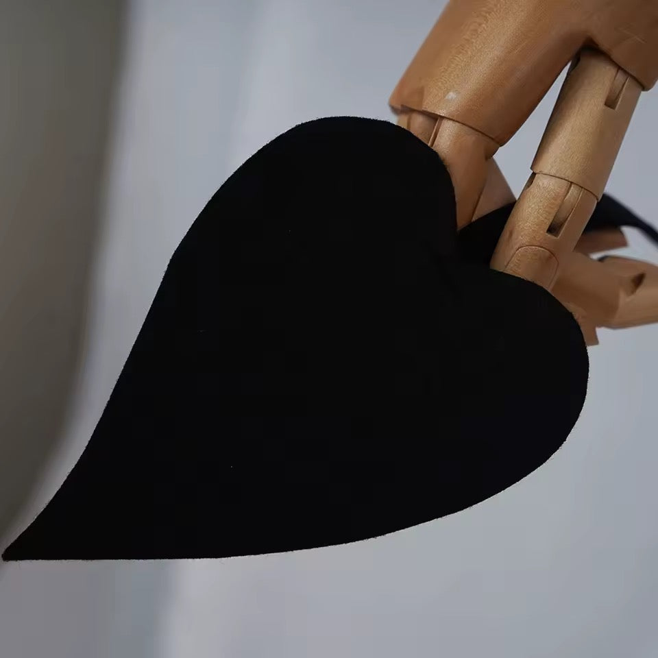Wooden mannequin hand holding a black heart-shaped object against a neutral background