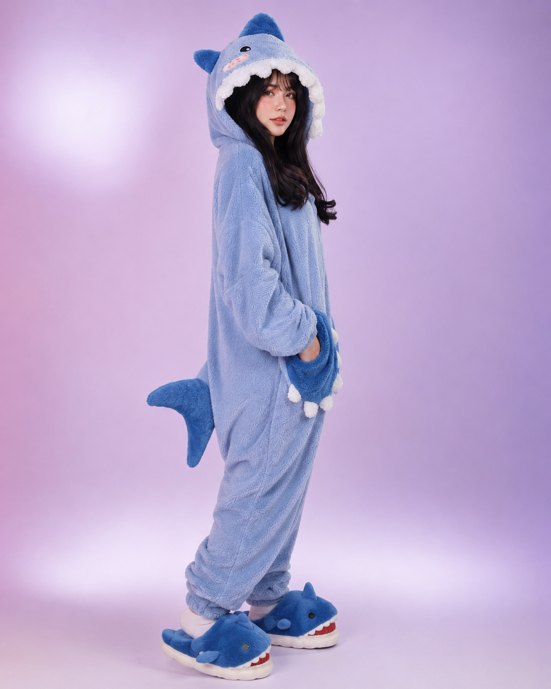 Person wearing a blue shark onesie against a light purple background