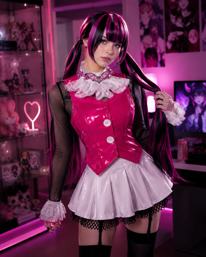 A person wearing a glossy hot pink and white anime-style costume with a pleated skirt, ruffled collar, sheer black sleeves, and long dark pink hair, standing in a pink-lit room with shelves and posters in the background.
