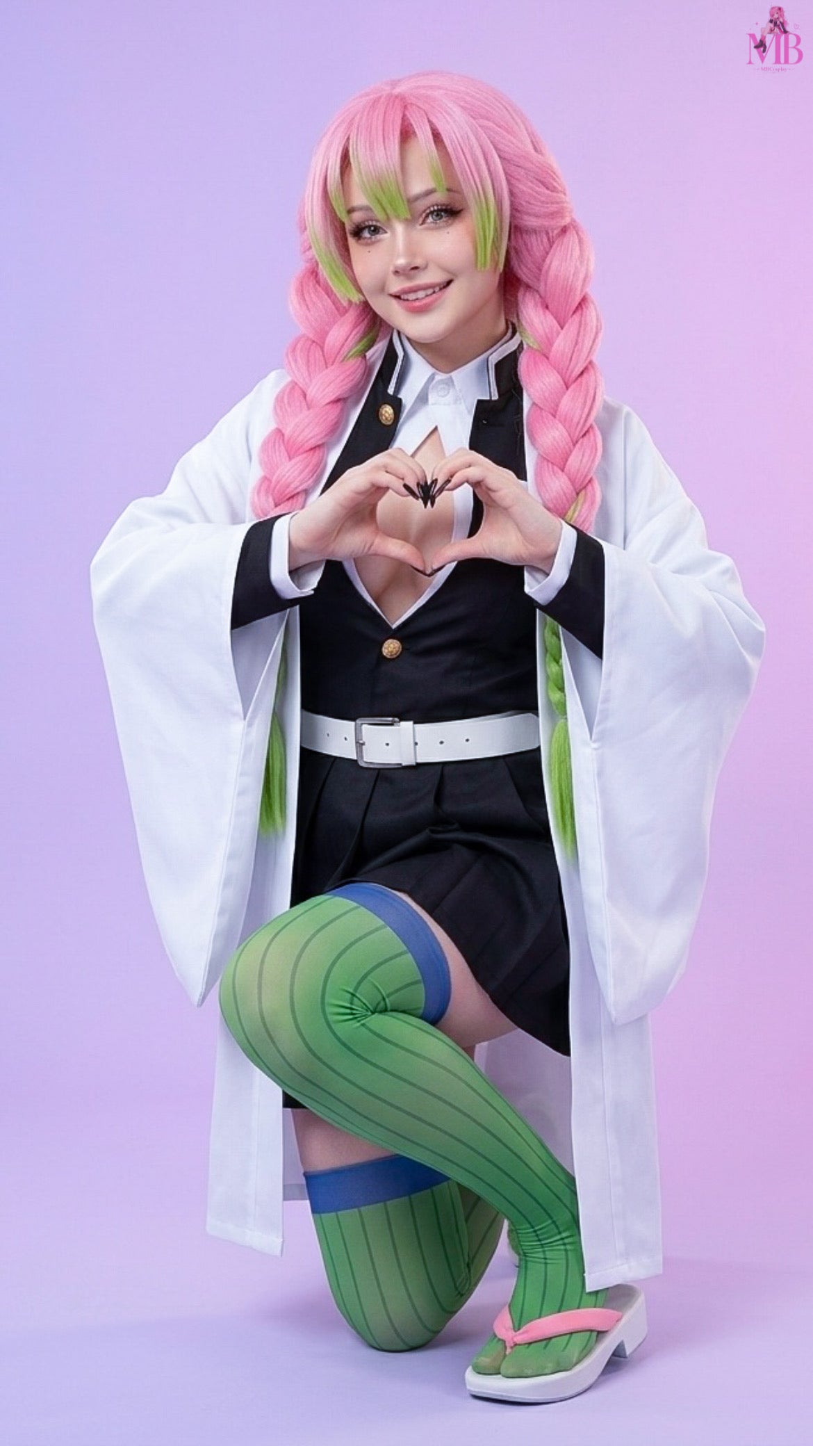 Kanroji Mitsuri Demon Slayer cosplay costume with optional pink and green braided wig in a kneeling heart pose, showcasing the authentic Love Hashira uniform, white haori, pleated skirt, thigh-high green socks, white belt and traditional sandals.