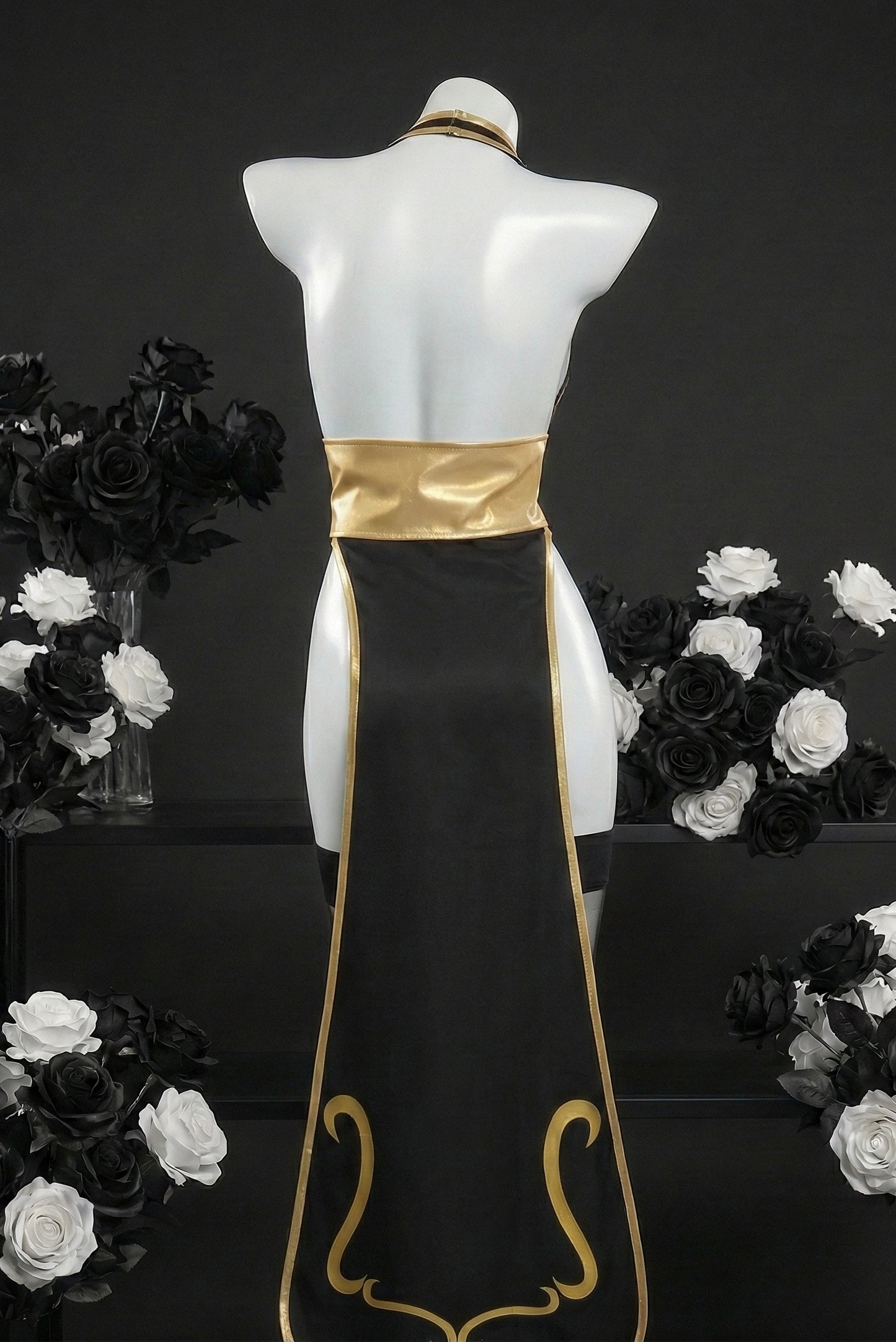 Mannequin wearing a black and gold dress with floral arrangements on a dark background