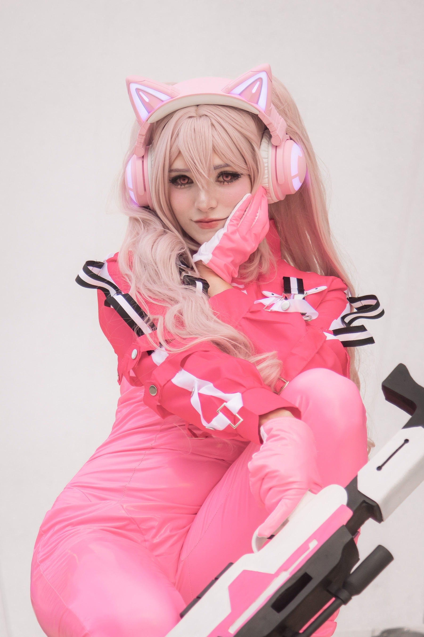 Close up of Alice cosplay from Nikke featuring pink cat-ear LED headset and matching tactical jumpsuit