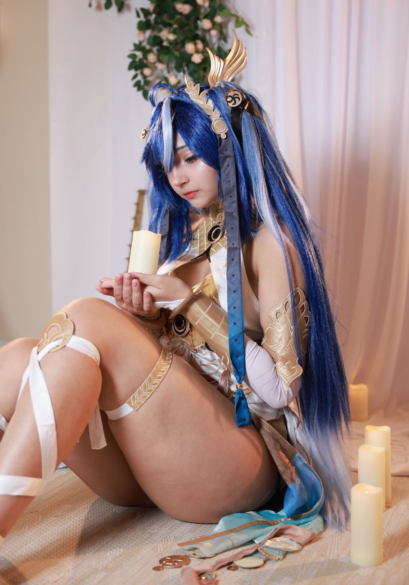 Person with blue hair and elaborate costume sitting on the floor with candles and decorative items.