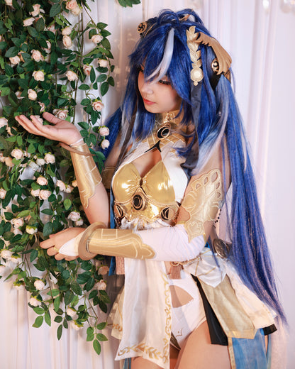High-detail portrait of a model in the Wuthering Waves Iuno Luno cosplay set posing by a white floral vine, showing the metallic gold arm guards, intricate gold collar, and vibrant blue twintail wig with white highlights