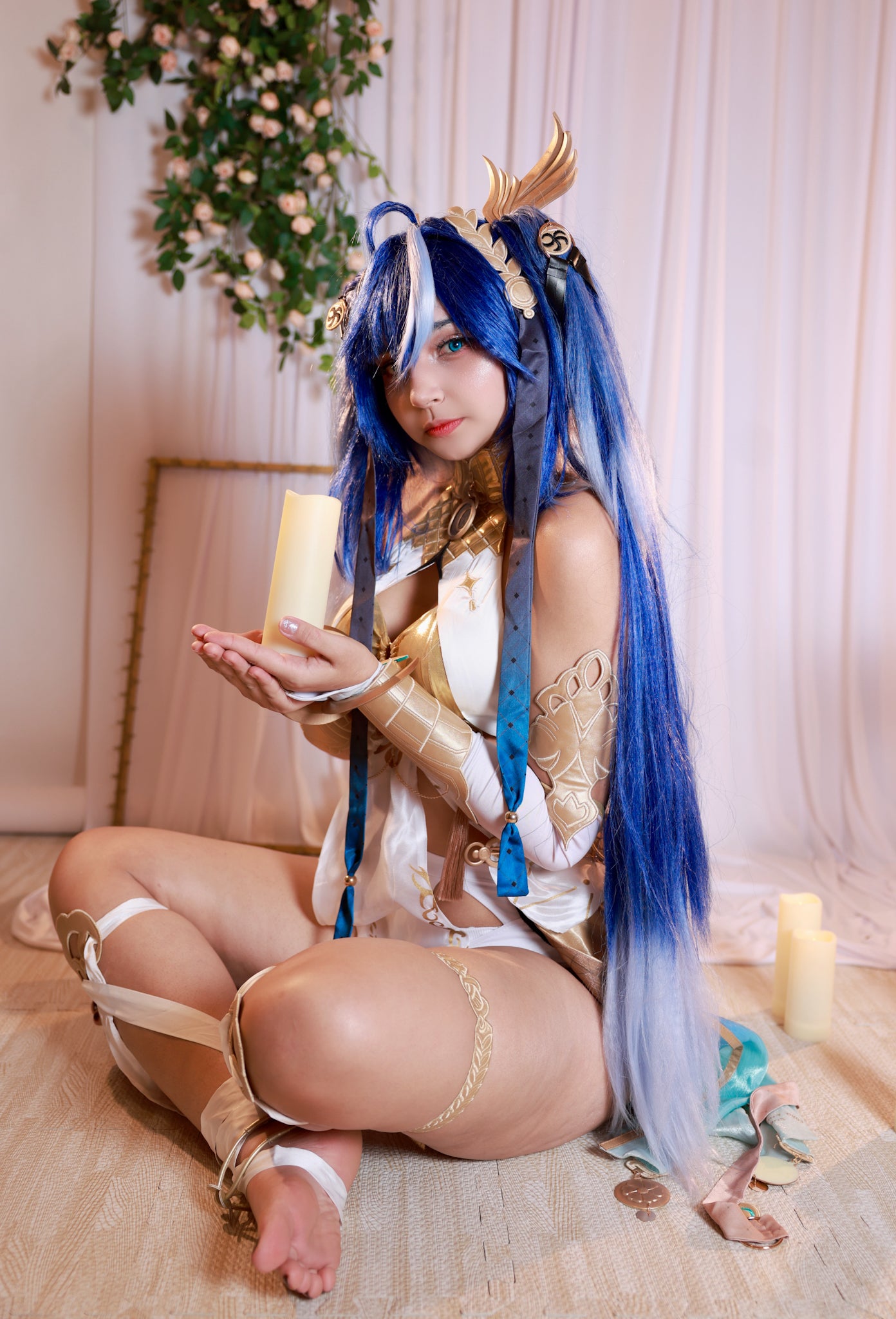 Aesthetic seated pose of a model in Wuthering Waves Iuno Luno cosplay holding a candle, highlighting the character-accurate metallic gold breastplate armor and matching gold leg ornaments.