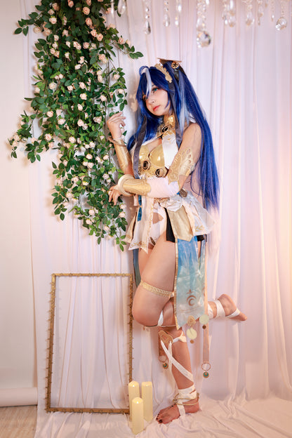 Person in elaborate costume with blue hair standing next to a decorative plant and framed mirror.